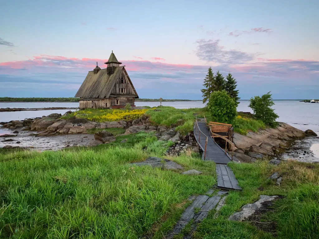 Edificio in legno consumato dalle intemperie con torre, situato su un paesaggio costiero roccioso in Carelia, immagine simbolica della regione culturale rurale della Russia settentrionale